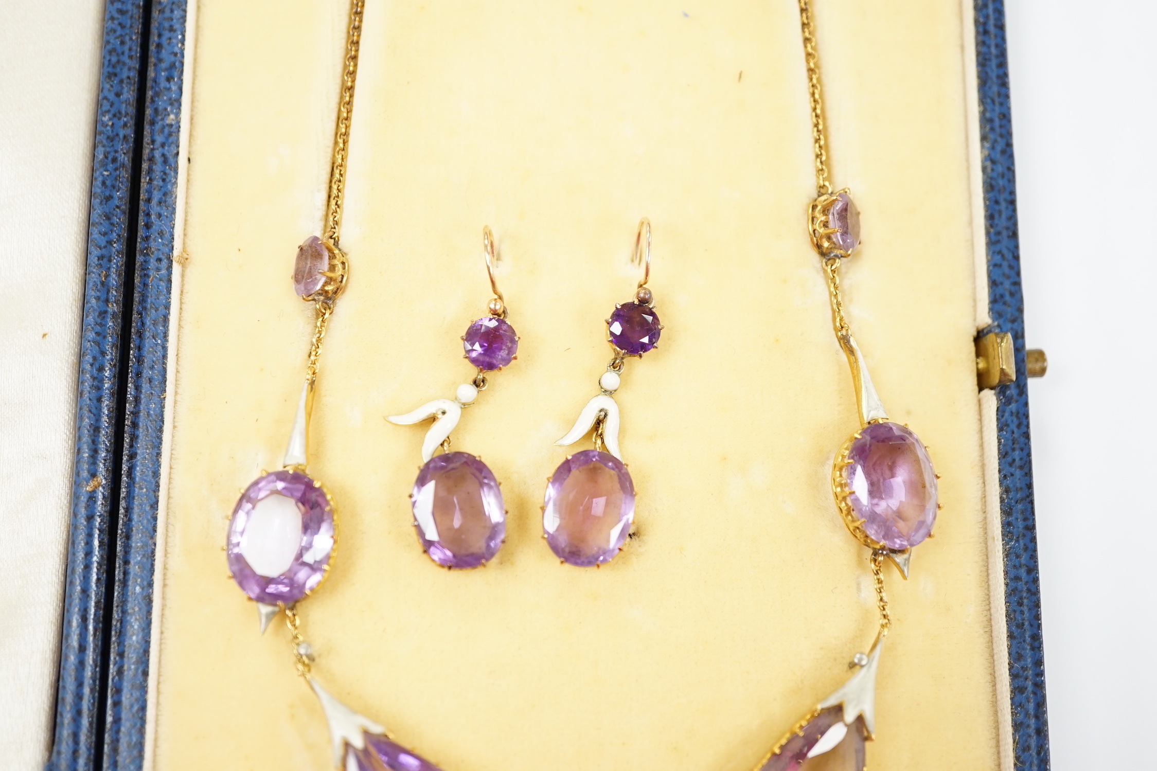 An early 20th century yellow metal, amethyst and enamel set suite of jewellery, comprising a drop necklace, 56cm and a par of matching drop earrings, 33mm, gross weight 38.1 grams.